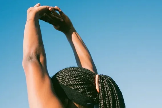 Back of woman's head with hair pulled up, arms stretched above her head, blue sky in the background